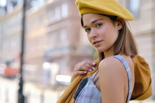 Photo of Close-up Fashion woman portrait of young pretty trendy girl posing at the city in Europe,summer street fashion, yellow beret , popular until the 60s.laughing and smiling portrait.trendy