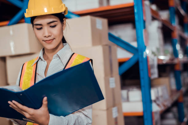 istock Engineer warehouse woman wearing a hardhat standing cargo at goods warehouse and check for control loading from Cargo freight ship for import and export by report on document. Teamwork concept 1272756846