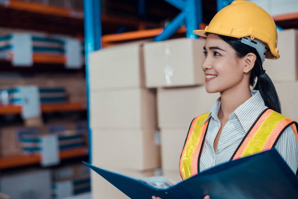 istock Engineer warehouse woman wearing a hardhat standing cargo at goods warehouse and check for control loading from Cargo freight ship for import and export by report on document. Teamwork concept 1272756849