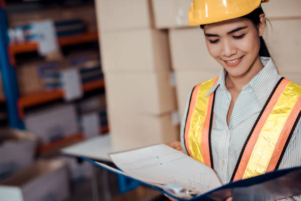 istock Engineer warehouse woman wearing a hardhat standing cargo at goods warehouse and check for control loading from Cargo freight ship for import and export by report on document. Teamwork concept 1272756851