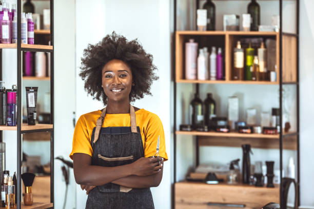 Stop by for the hippest haircuts in the city Smiling African American female barber standing with arms crossed in hair salon. Portrait of confident young woman is working at barber shop hair stylist stock pictures, royalty-free photos & images