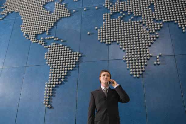istock Business man using mobile phone in front of world map in office 1272757078