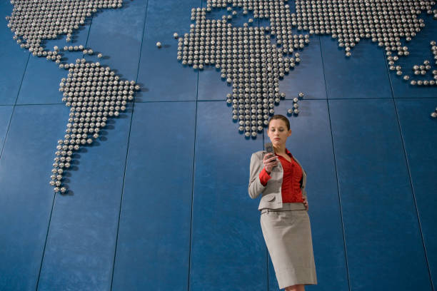 istock Business woman text messsaging using mobile phone in front of world map in office 1272757322