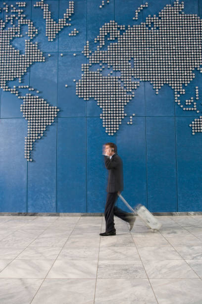 Business man with suitcase using mobile phone while walking past world map on wall