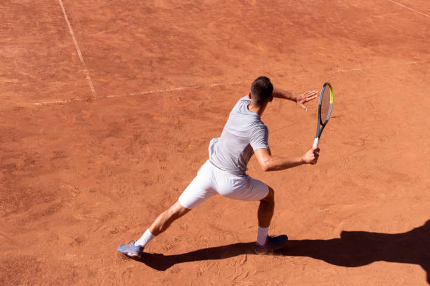 Professional tennis player performs forehand hit on clay tennis court. Young male athlete with tennis racket in action. Junior tennis sport. Back view, shadow, copy space Professional tennis player performs forehand hit on clay tennis court. Young male athlete with tennis racket in action. Junior tennis sport. Back view, shadow, copy space Tennis stock pictures, royalty-free photos & images