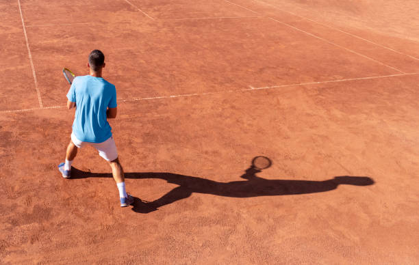 tenisista i jego cień na czerwonym kortach tenisowych. profesjonalny tenisista jest gotowy do odbioru piłki. początek meczu tenisowego. tło sportowe. kopiowanie miejsca na tekst - match sport sport outdoors teenagers only zdjęcia i obrazy z banku zdjęć