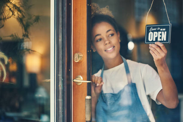 Coffee lovers, I'm here for you Shot of a young woman hanging an open sign on the window of a cafe open photos stock pictures, royalty-free photos & images