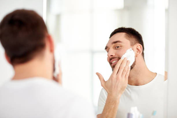 istock happy man applying shaving foam at bathroom mirror 1272760864