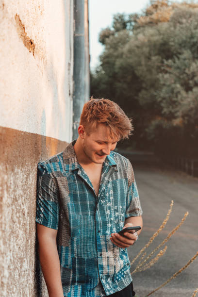 Young man leaning on old wall checking messages on mobile phone
