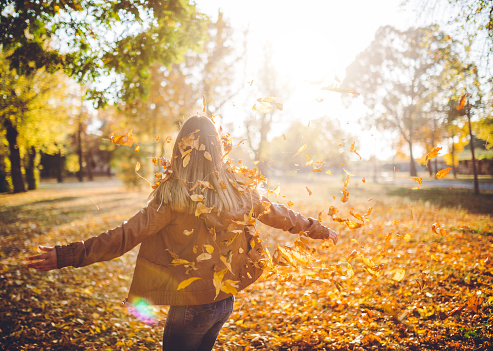 Young beautiful Caucasian woman standing in autumn leaves and throwing them in the air.