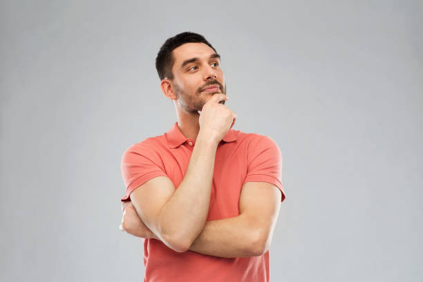 man in polo t-shirt thinking over gray background - uncertainty imagens e fotografias de stock