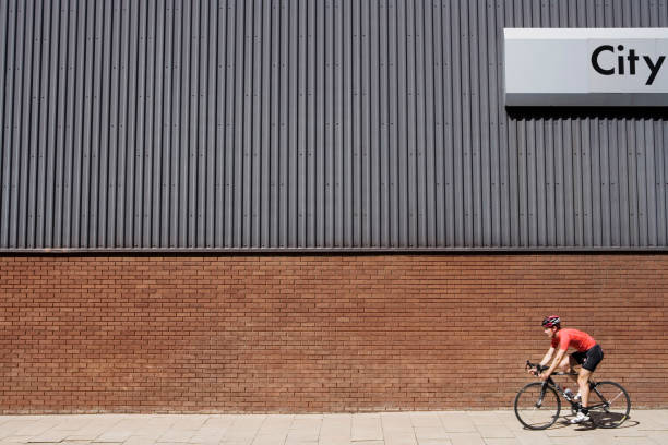 istock Man cycling past building with 'City' written on side 1272762442
