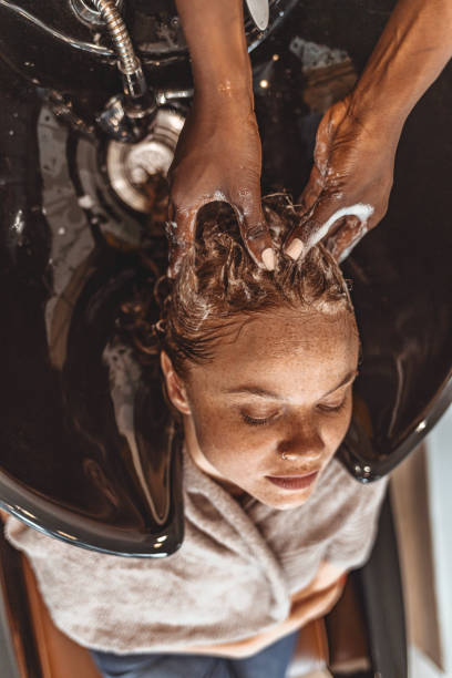 At the hairdresser Washing procedure. Female redhead Client is resting while its hair is being washed. black woman washing hair stock pictures, royalty-free photos & images