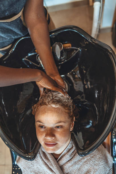 Young woman enjoys shampoo at salon Woman applying shampoo and massaging hair of a customer. Woman having her hair washed in a hairdressing salon. black woman washing hair stock pictures, royalty-free photos & images