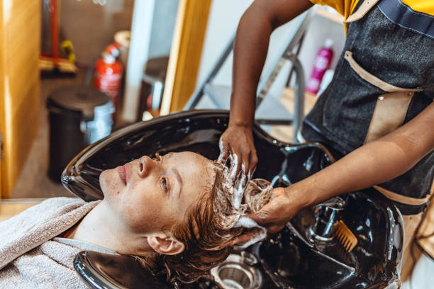 Woman getting hair shampooed at salon Woman applying shampoo and massaging hair of a customer. Woman having her hair washed in a hairdressing salon. black woman washing hair stock pictures, royalty-free photos & images