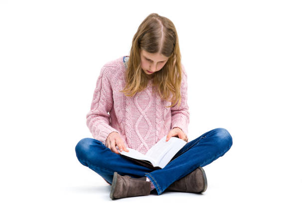 istock Young, blond girl is sitting and reading interesting book from her home library. 1272769161