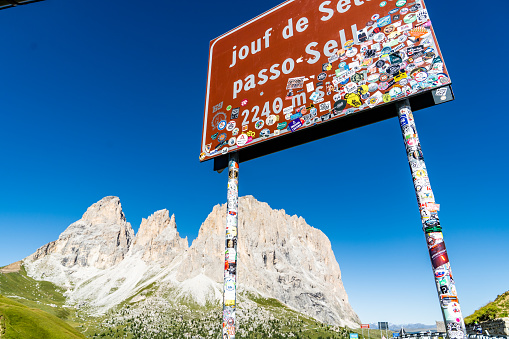 Passo Sella road sign with travelers stickers. Italian Alps on the background.