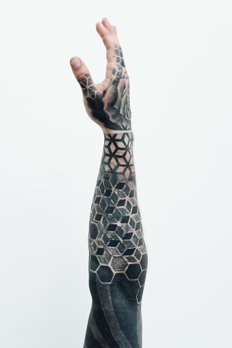Creative arm sleeve tattoo. Conceptual shot of tattooed male arm reaching up against white background