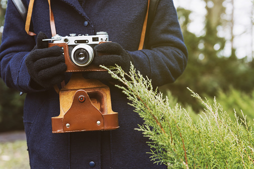 Close up of young woman hipster holding retro film camera in hands. Woman's hands holding an old retro camera at nature background.