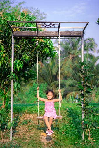 Little girl in pink dress sitting on a swing in the park
