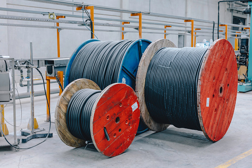 Large and red colour wooden cable spools stands in large electronic cable factory warehouse indoor