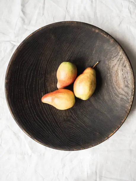 Ripe red-yellow pears lie in large brown wooden bowl on white background. Top view