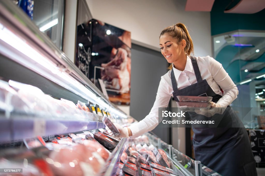 Supermarket worker organizing position in meat department. Placing meat in order. Working in grocery store. Supermarket Stock Photo