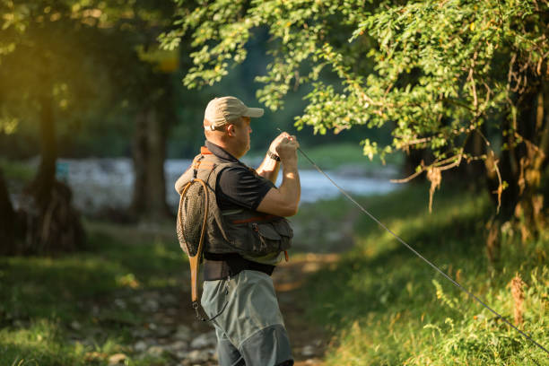 Fisherman is getting ready to start fishing in a mountain river. He is wearing special clothes and he has fishing equipment. stock photo