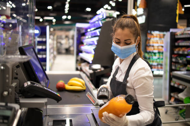 Cashier in supermarket wearing mask and gloves fully protected against corona virus. Working during covid-19 pandemic. Cashier in supermarket wearing mask and gloves fully protected against corona virus. Working during covid-19 pandemic. cashier photos stock pictures, royalty-free photos & images