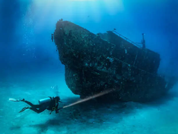 A scuba diver with a torch explores a sunken shipwreck at the seabed of the Maldives islands, Indina Ocean