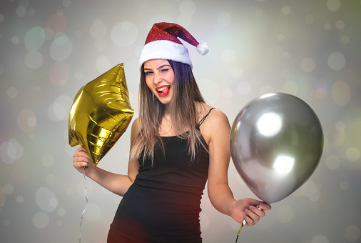 Portrait Of A Young Beautiful Woman With Santa Claus Hat Holding Air Balloons And Dancing, New Year Celebration Concept