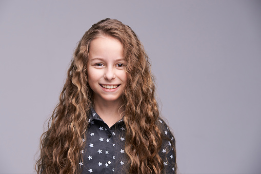 Prety little smile woman. Curly long hair. Nice young girl studio portrait. Adorable haircut. Grey background with copyspace. Positive lifestyle.