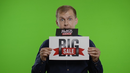 Man shopper holding Black Friday Deals advertisement in his month and showing Big Sale inscription. Guy looking shocked amazed of discounts and low prices. Chroma key background
