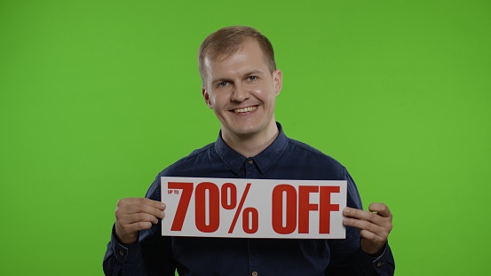 Happy smiling man showing Up To 70 percent Off inscriptions signs, rejoicing good discounts, low prices for online shopping sales. Studio shot on chroma key background