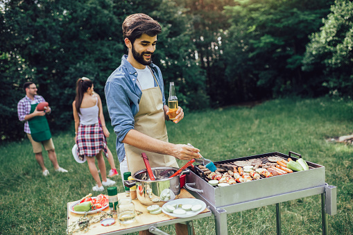 Handsome male preparing barbecue outdoors for friends