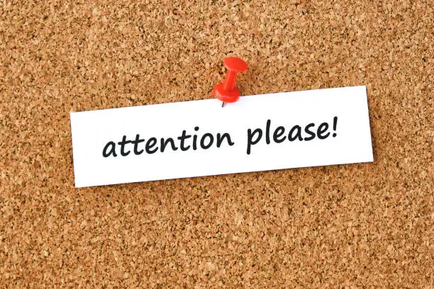 Attention please. Text written on a piece of paper or note, cork board background.