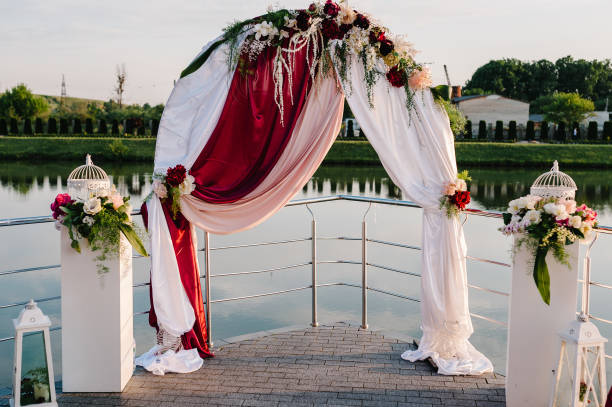 istock Setup wedding ceremony on pier. Wedding arch decorated with flowers. Wedding atmosphere, scenery, celebration. Photography, concept. 1272797048