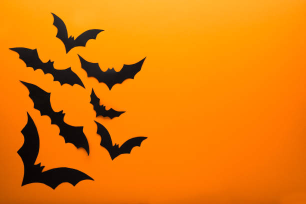 istock Halloween and decoration concept - black paper bats flying over orange background. Copy space. 1272806624
