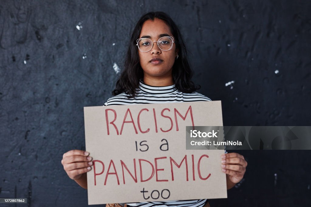 Nothing right about racism Studio shot of a young woman protesting against racism against a dark background Racism Stock Photo