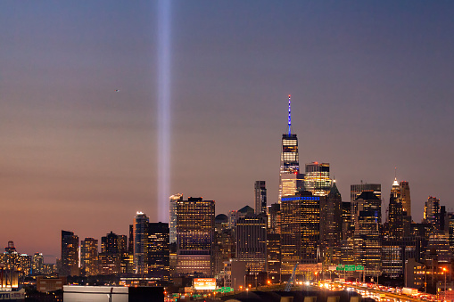 New York, New York - September 11, 2020 : The 9/11 tribute lights seen next to One World Trade, with car light trails from Interstate 278 (I-278) heading towards Manhattan.