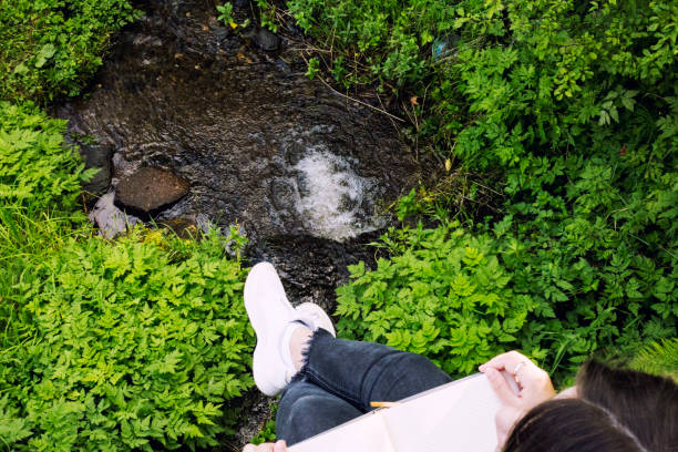 Young woman reading book near stream