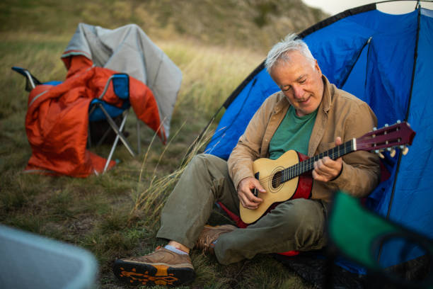 istock Senior man sitting in front of tent and playing guitar while camping 1272821253