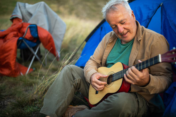 istock Senior man sitting in front of tent and playing guitar while camping 1272821268