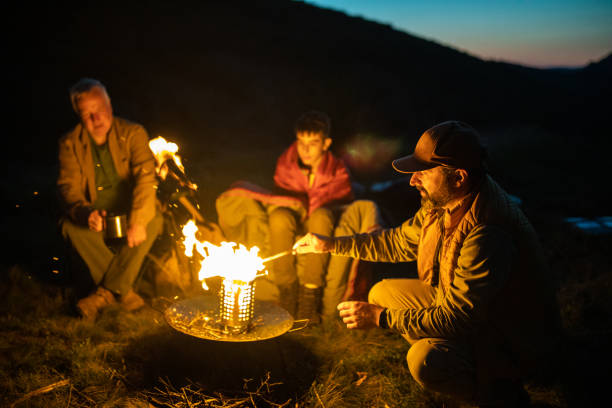 istock Multi-generation family sitting around campfire on mountain at evening 1272821882