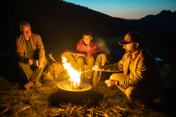 istock Multi-generation family sitting around campfire on mountain at evening 1272822137