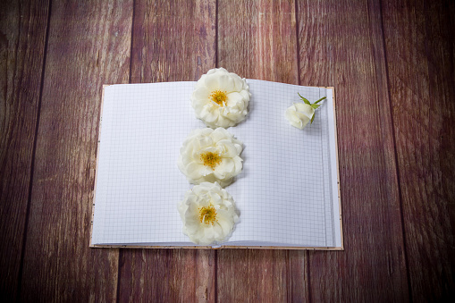 bouquet of beautiful white roses and blank notebook on a wooden table