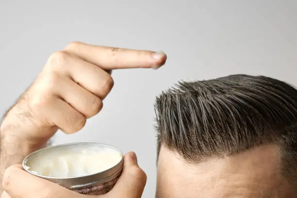 Man applying a clay, pomade, wax, gel or mousse from round metal box for styling his hair after barbershop hair cut. Advertising concept of mans products. Treatment and care against lost of hair.