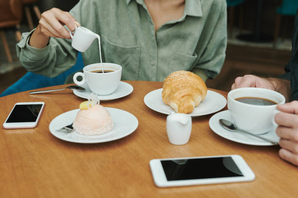 istock Concentrated young bearded man in casual shirt drinking coffee and eating croissant while checking smartphone in cafe 1272832507