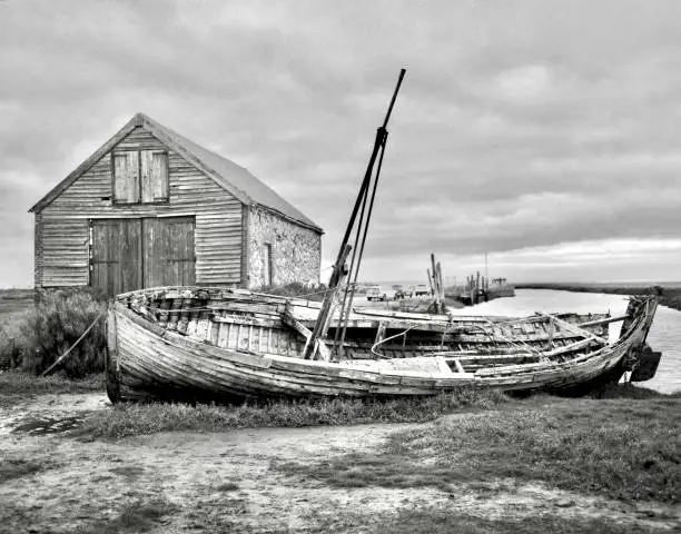 Monochrome view of disused fishing boat onNorfolk salt flats and disused boathouse