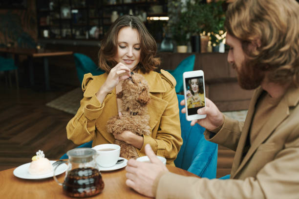 istock Busy young bearded man sitting at table in modern cafe and drinking coffee while discussing project by phone 1272835547